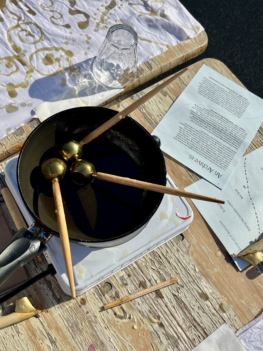 Tjanting pens resting in a pan of melted wax beside the workshop notes