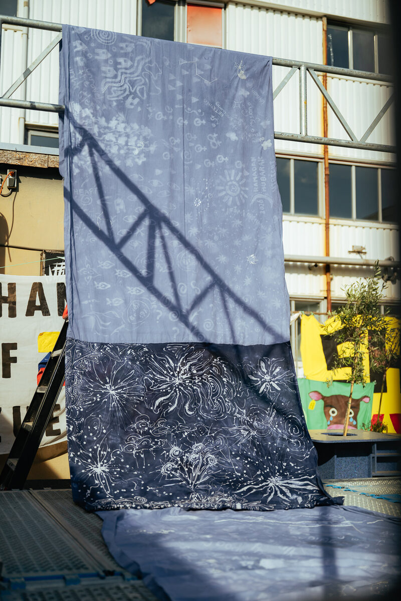 Finished batik hanging from the scaffold, white drawings glowing against indigo
