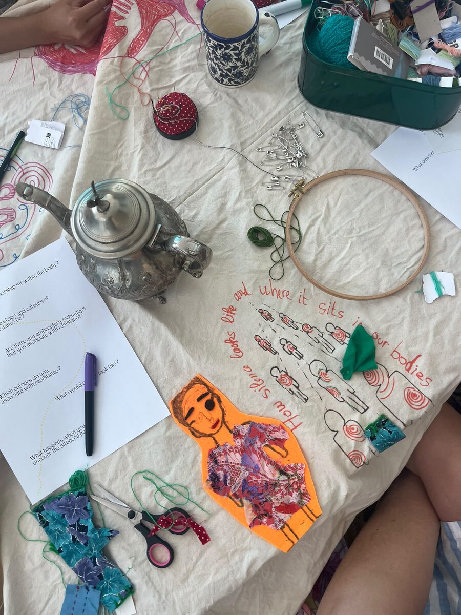 Workshop table with embroidery hoop, drawings and teapot