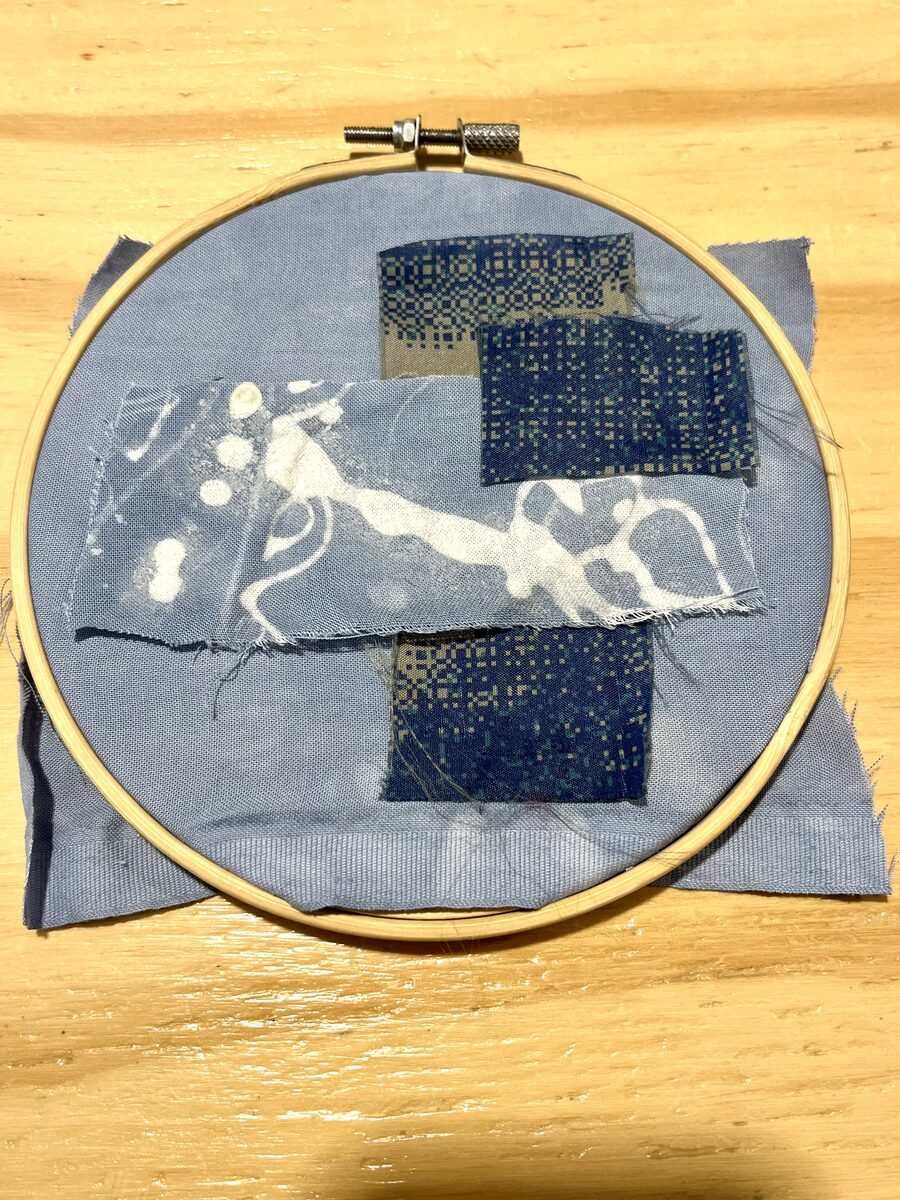 Embroidery hoop holding layered blue fabric patches